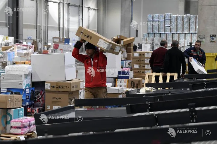 Un muncitor transportă cutii într-un depozit aglomerat.