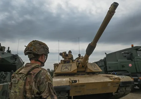 Soldat observând un tanc modern în cadrul exercițiilor militare.