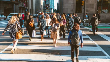 Oameni traversând o stradă aglomerată într-un oraș modern.