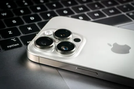 Un smartphone Apple cu trei camere pe un laptop gri.