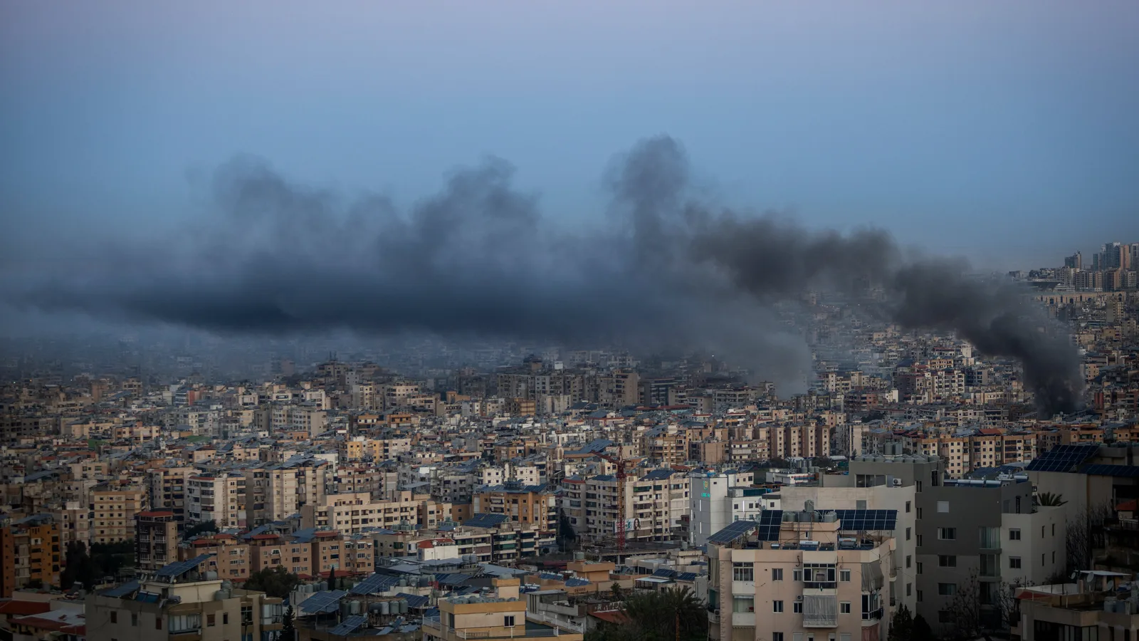 Fum negru se ridică deasupra orașului, semn al distrugerii recente.