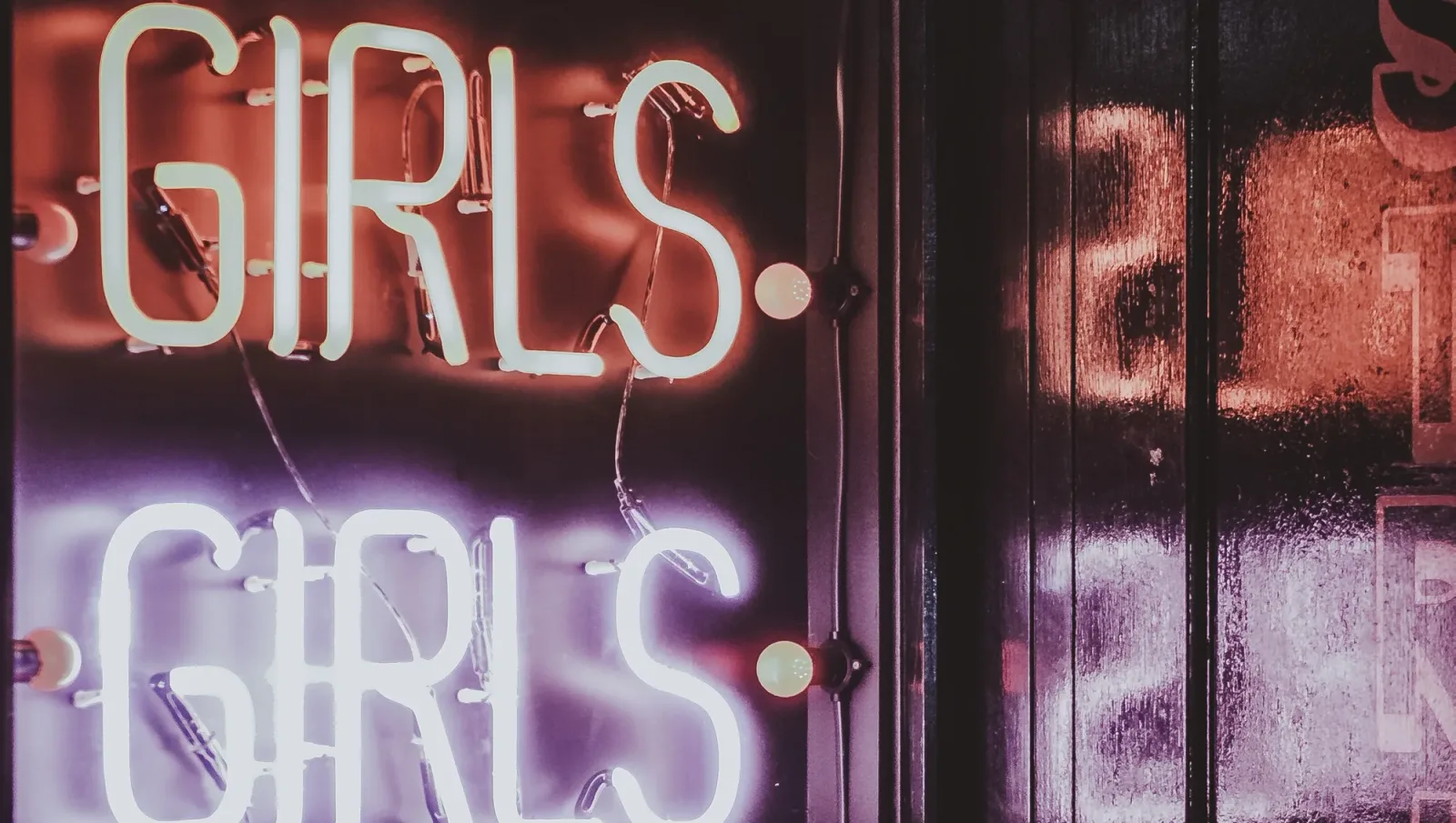 Neon cuvântul „Girls” pe un fundal întunecat, simbolizând activități de natură sexuală.