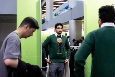 Un bărbat probează un pulover cu caricatura unui CEO în fața oglinzii.