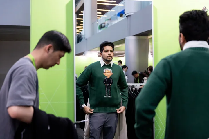 Un bărbat probează un pulover cu caricatura unui CEO în fața oglinzii.