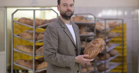 Un bărbat ținând o pâine artizanală într-o brutărie modernă.