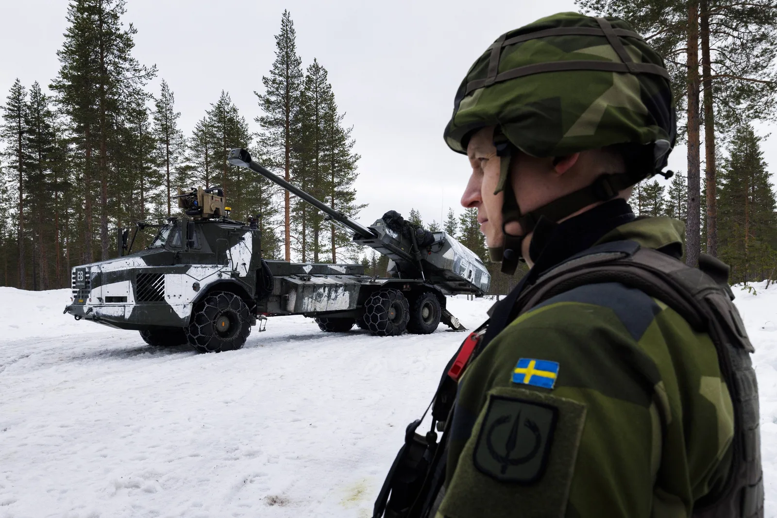 Soldat suedez în fața unui vehicul militar pe zăpadă.