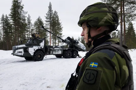 Soldat suedez în fața unui vehicul militar pe zăpadă.