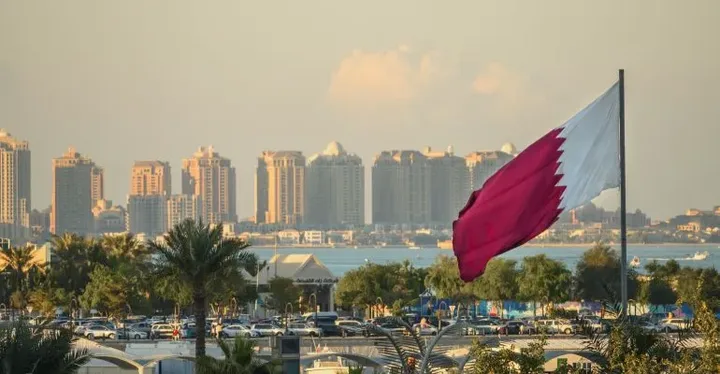 Steagul Qatarului fluturând în fața unui peisaj urban modern.
