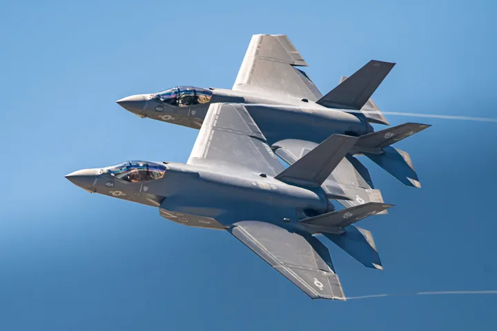 Două avioane F-35 zburând în formare pe un fundal albastru.