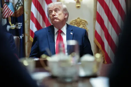 Donald Trump în timpul unei întâlniri oficiale, cu steagurile SUA în fundal.