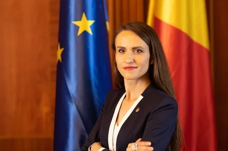 Oana Țoiu, ministra, în fața drapelului României și UE.